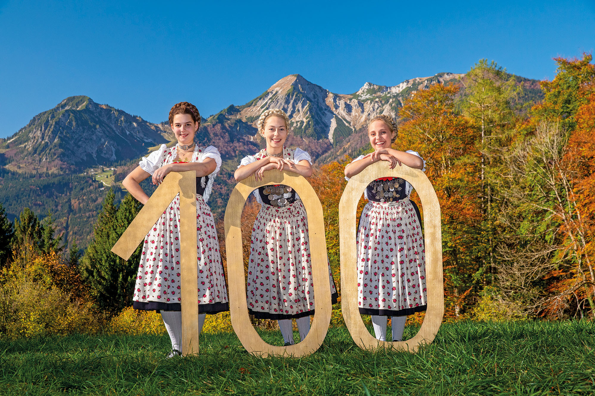 Gamsgebirlger zeigen ein Schild mit der Zahl 100, Alpen im Hintergrund